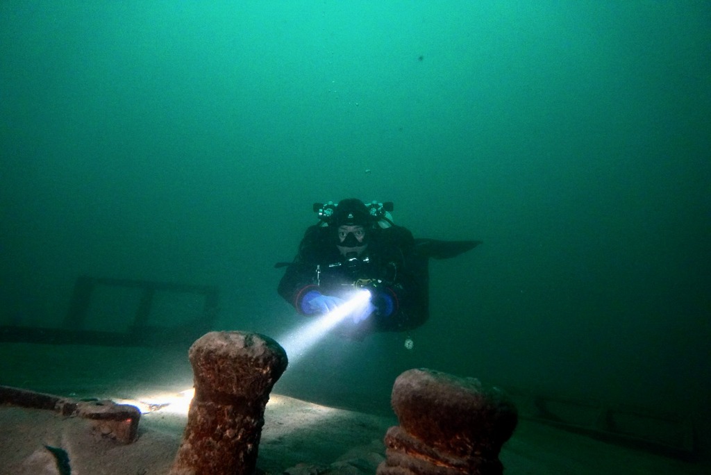 A diver with a dive light examining a historic cargo wreck in Walensee